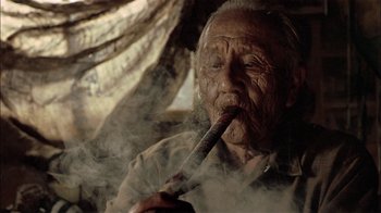 Movie still from “Thunderheart” (1992), directed by Michael Apted – An old man smoking a cigarette while sitting in a chair; Close Up shot, Low angle