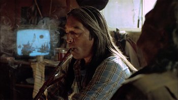 Movie still from “Thunderheart” (1992), directed by Michael Apted – A man with long black hair is smoking a pipe; Close Up shot, Low angle