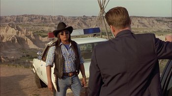 Movie still from “Thunderheart” (1992), directed by Michael Apted – A man in a cowboy hat and a jacket talking to a man in a suit and tie; Medium shot, Over the shoulder angle