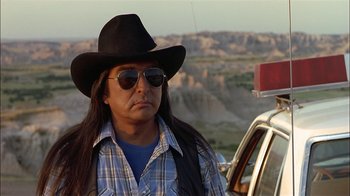 Movie still from “Thunderheart” (1992), directed by Michael Apted – A man with long hair wearing a cowboy hat and sunglasses; Close Up shot, Over the shoulder angle