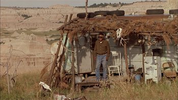 Movie still from “Thunderheart” (1992), directed by Michael Apted – A man standing in front of a shack in a field; Wide shot, Low angle