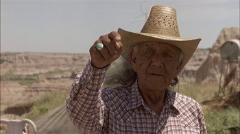 Movie still from “Thunderheart” (1992), directed by Michael Apted – An old man wearing a straw hat holding something; Close Up shot, Low angle