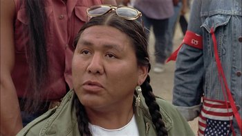Movie still from “Thunderheart” (1992), directed by Michael Apted – A man with long hair and a beard wearing sunglasses; Close Up shot, Over the shoulder angle