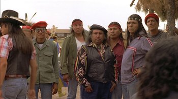 Movie still from “Thunderheart” (1992), directed by Michael Apted – A group of men standing next to each other on a beach; Medium shot, Over the shoulder angle