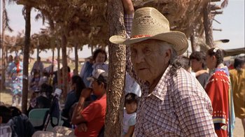 Movie still from “Thunderheart” (1992), directed by Michael Apted – An old man wearing a hat standing next to a tree; Medium shot, Over the shoulder angle
