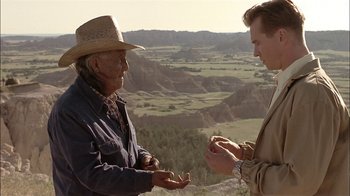 Movie still from “Thunderheart” (1992), directed by Michael Apted – A man in a cowboy hat and a man in a suit are talking to each other on a hill; Medium shot, Over the shoulder angle