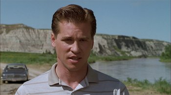 Movie still from “Thunderheart” (1992), directed by Michael Apted – A person wearing a polo shirt near a body of water; Close Up shot, Over the shoulder angle