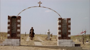 Movie still from “Thunderheart” (1992), directed by Michael Apted – A man riding a horse down a dirt road under a cross; Extreme Wide shot, Low angle