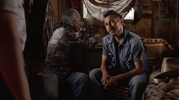 Movie still from “Thunderheart” (1992), directed by Michael Apted – A man sitting next to another man in a room; Medium shot, Over the shoulder angle
