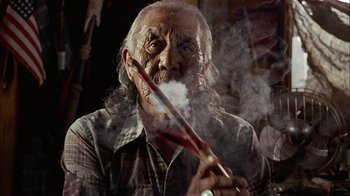 Movie still from “Thunderheart” (1992), directed by Michael Apted – An old man smoking a pipe with smoke coming out of his mouth; Close Up shot, Low angle