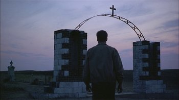 Movie still from “Thunderheart” (1992), directed by Michael Apted – A man standing in front of an arch with a cross on it; Wide shot, Low angle