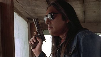 Movie still from “Thunderheart” (1992), directed by Michael Apted – A man with long hair and sunglasses holding a gun; Close Up shot, Low angle