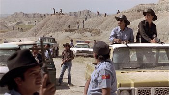 Movie still from “Thunderheart” (1992), directed by Michael Apted – A group of people standing around a dirt field; Wide shot, Over the shoulder angle