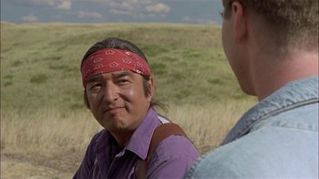 Movie still from “Thunderheart” (1992), directed by Michael Apted – A man with a bandana around his head talking to another man in a field; Close Up shot, Over the shoulder angle