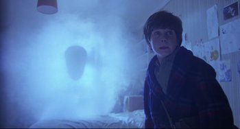 Movie still from “Time Bandits” (1981), directed by Terry Gilliam – A young boy standing next to a bed in front of smoke; Medium shot, Over the shoulder angle