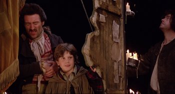 Movie still from “Time Bandits” (1981), directed by Terry Gilliam – A young boy standing next to a wooden pole; Medium shot, Over the shoulder angle