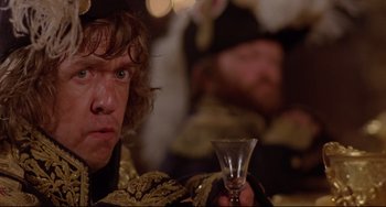 Movie still from “Time Bandits” (1981), directed by Terry Gilliam – A man holding a wine glass in his right hand; Close Up shot, Over the shoulder angle