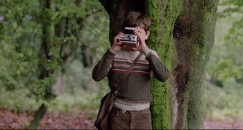 Movie still from “Time Bandits” (1981), directed by Terry Gilliam – A young boy taking a picture of himself with a camera; Medium shot, Low angle