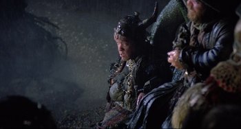 Movie still from “Time Bandits” (1981), directed by Terry Gilliam – A man sitting on top of a chair next to another man; Medium shot, Over the shoulder angle