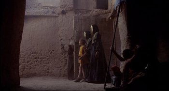 Movie still from “Time Bandits” (1981), directed by Terry Gilliam – A group of people standing next to each other near a building; Wide shot, Over the shoulder angle