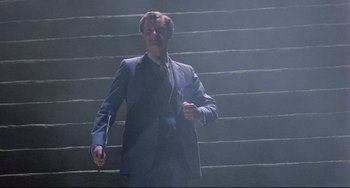 Movie still from “Time Bandits” (1981), directed by Terry Gilliam – A man in a suit and tie walking up a set of stairs; Medium shot, Low angle