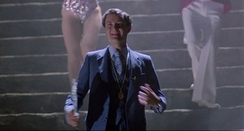 Movie still from “Time Bandits” (1981), directed by Terry Gilliam – A man in a blue suit holding a microphone; Medium shot, Low angle