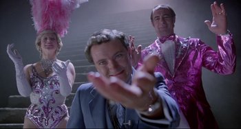 Movie still from “Time Bandits” (1981), directed by Terry Gilliam – A man in a suit and a pink suit is holding his hands up; Medium shot, Low angle