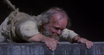 Movie still from “Time Bandits” (1981), directed by Terry Gilliam – An old man with long grey hair and a long white beard leaning on a wall; Close Up shot, Low angle