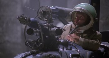 Movie still from “Time Bandits” (1981), directed by Terry Gilliam – A man in a helmet is working on a machine; Medium shot, High angle