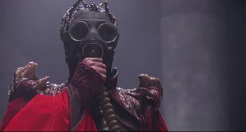 Movie still from “Time Bandits” (1981), directed by Terry Gilliam – A person wearing a gas mask and holding a pipe; Medium shot, Low angle