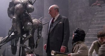 Movie still from “Time Bandits” (1981), directed by Terry Gilliam – An older man in a suit and tie standing next to another man in a suit; Medium shot, Over the shoulder angle