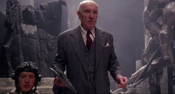 Movie still from “Time Bandits” (1981), directed by Terry Gilliam – An older man in a suit and tie holding a knife; Medium shot, Low angle