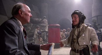 Movie still from “Time Bandits” (1981), directed by Terry Gilliam – A man in a suit is holding a baseball bat and talking to another man in a uniform; Medium shot, Over the shoulder angle