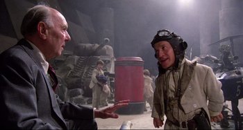 Movie still from “Time Bandits” (1981), directed by Terry Gilliam – A man in a helmet talking to another man in a suit; Medium shot, Over the shoulder angle