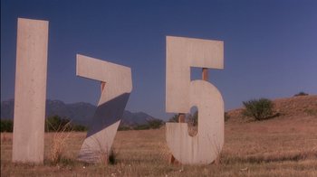 Movie still from “Tin Cup” (1996), directed by Ron Shelton – A number sign sitting in the middle of a grassy field; Extreme Wide shot, Low angle