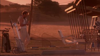 Movie still from “Tin Cup” (1996), directed by Ron Shelton – A woman standing next to an empty chair; Wide shot, Over the shoulder angle
