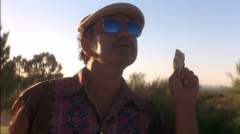 Movie still from “Tin Cup” (1996), directed by Ron Shelton – A man in a hat and sunglasses holding a piece of food; Close Up shot, Low angle
