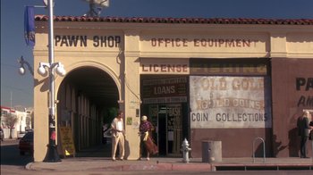 Movie still from “Tin Cup” (1996), directed by Ron Shelton – Two people are standing in front of an antique store; Extreme Wide shot, Low angle