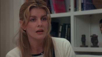 Movie still from “Tin Cup” (1996), directed by Ron Shelton – A person sitting in a room near a bookshelf; Close Up shot, Over the shoulder angle