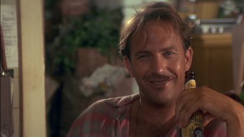 Movie still from “Tin Cup” (1996), directed by Ron Shelton – A person smiling with a bottle; Close Up shot, Low angle