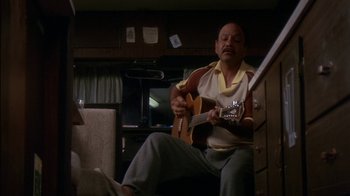 Movie still from “Tin Cup” (1996), directed by Ron Shelton – A man sitting in a chair playing a guitar; Medium shot, Low angle