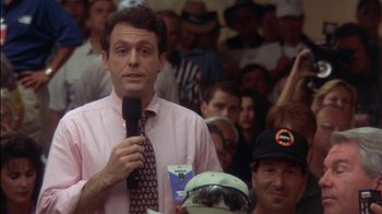 Movie still from “Tin Cup” (1996), directed by Ron Shelton – A man is holding a microphone in front of a group of people; Close Up shot, High angle