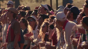 Movie still from “Tin Cup” (1996), directed by Ron Shelton – A group of people standing in a crowd holding cups; Medium shot, High angle