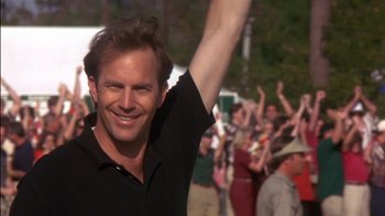 Movie still from “Tin Cup” (1996), directed by Ron Shelton – A man raising his arm in the air while standing in front of a group of onlookers; Close Up shot, Low angle