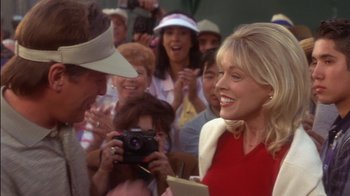 Movie still from “Tin Cup” (1996), directed by Ron Shelton – A group of people standing around a woman holding a camera; Close Up shot, Over the shoulder angle