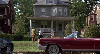 Movie still from “Tin Men” (1987), directed by Barry Levinson – Two people standing in front of a house and a car; Wide shot, Low angle