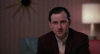 Movie still from “Tin Men” (1987), directed by Barry Levinson – A man wearing a suit and tie sitting in a room; Close Up shot, Low angle