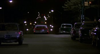 Movie still from “Tin Men” (1987), directed by Barry Levinson – A group of cars driving down a street at night; Extreme Wide shot, Low angle