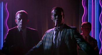 Movie still from “Tin Men” (1987), directed by Barry Levinson – A man in a suit and tie holding a microphone in front of another man in a suit and tie; Medium shot, Low angle