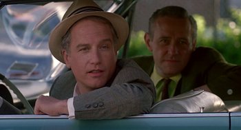 Movie still from “Tin Men” (1987), directed by Barry Levinson – A man in a suit and a hat sitting in a car next to another man in a suit; Close Up shot, Over the shoulder angle